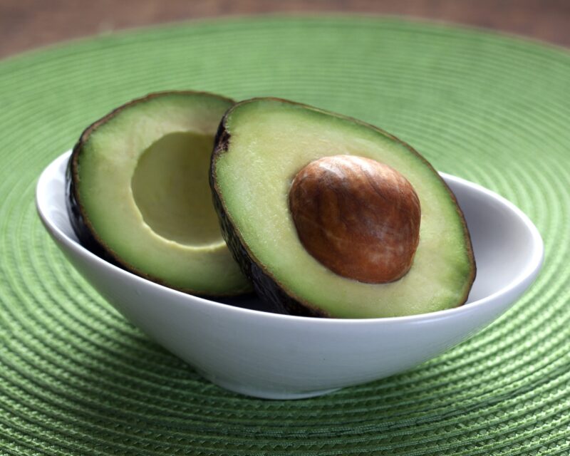 avocado halves in white bowl on green woven placement, grilled corn with avocado crema, recipe, ppma
